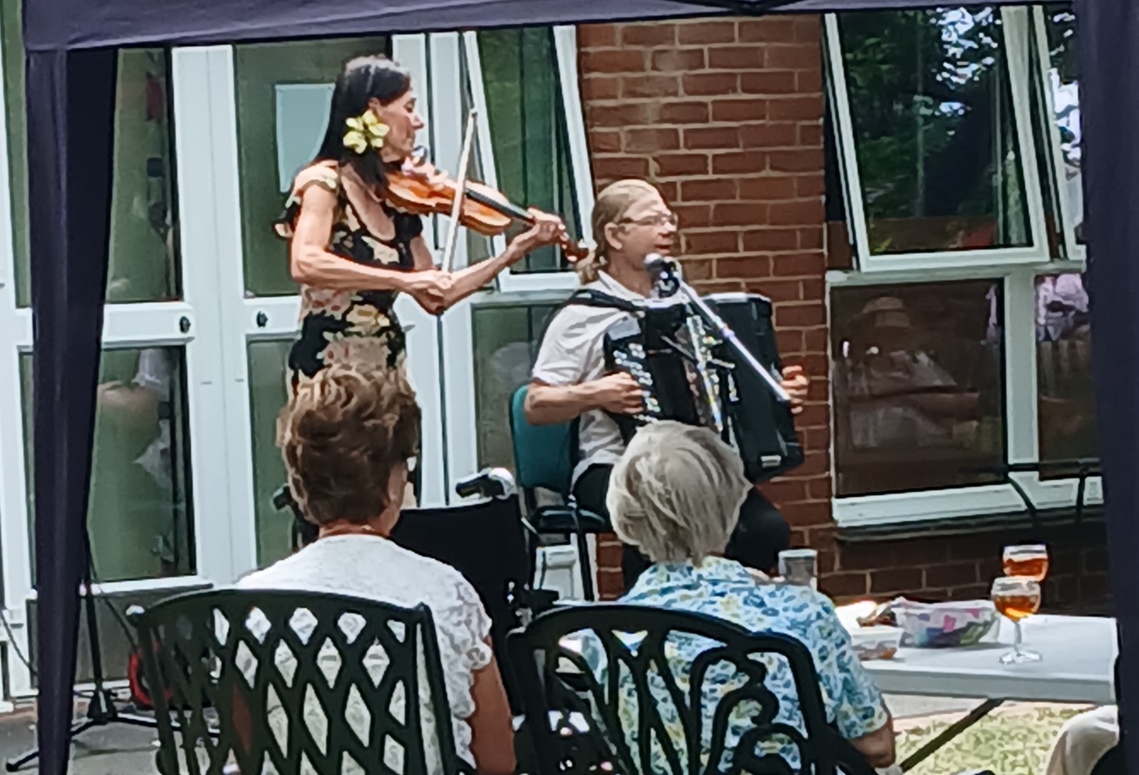 Sarah violin and Igor accordion entertain two ladies seated with glasses of Pimm's