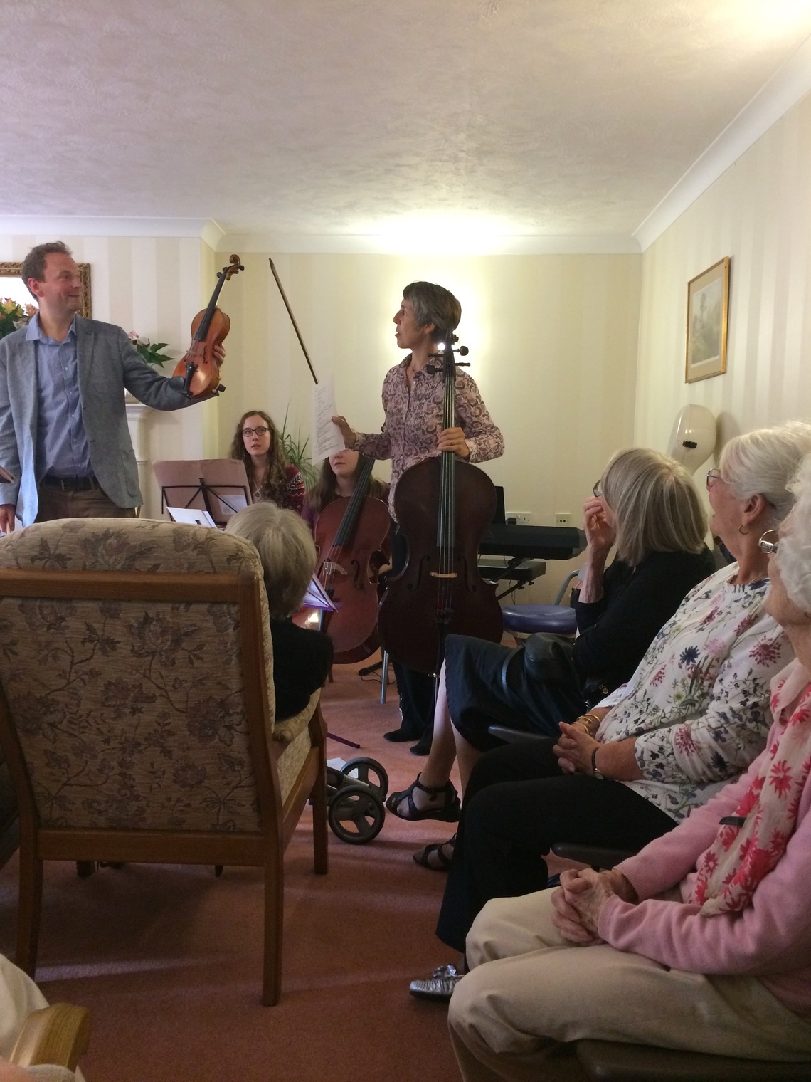 Nigel holds up his "peanut" violin to compare its size and shape against Sarah's cello at a care home in Bromley
