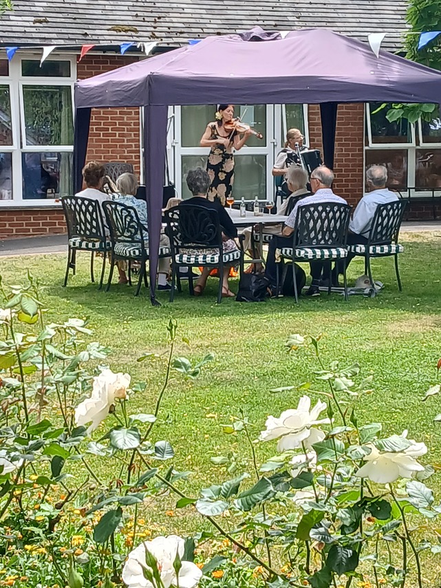 Music wafts across the lawn past audience under the gazebo